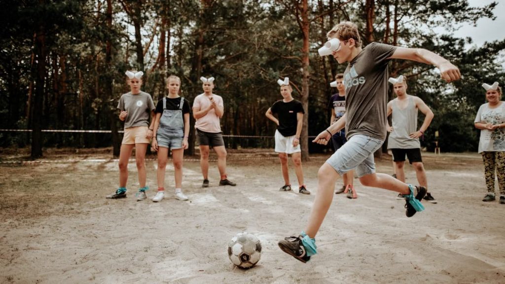 Teenagers enjoying an outdoor soccer game with a humorous twist using eyecovers as a challenge.