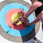 A female archer inspects arrows on a target after a shooting session outdoors.